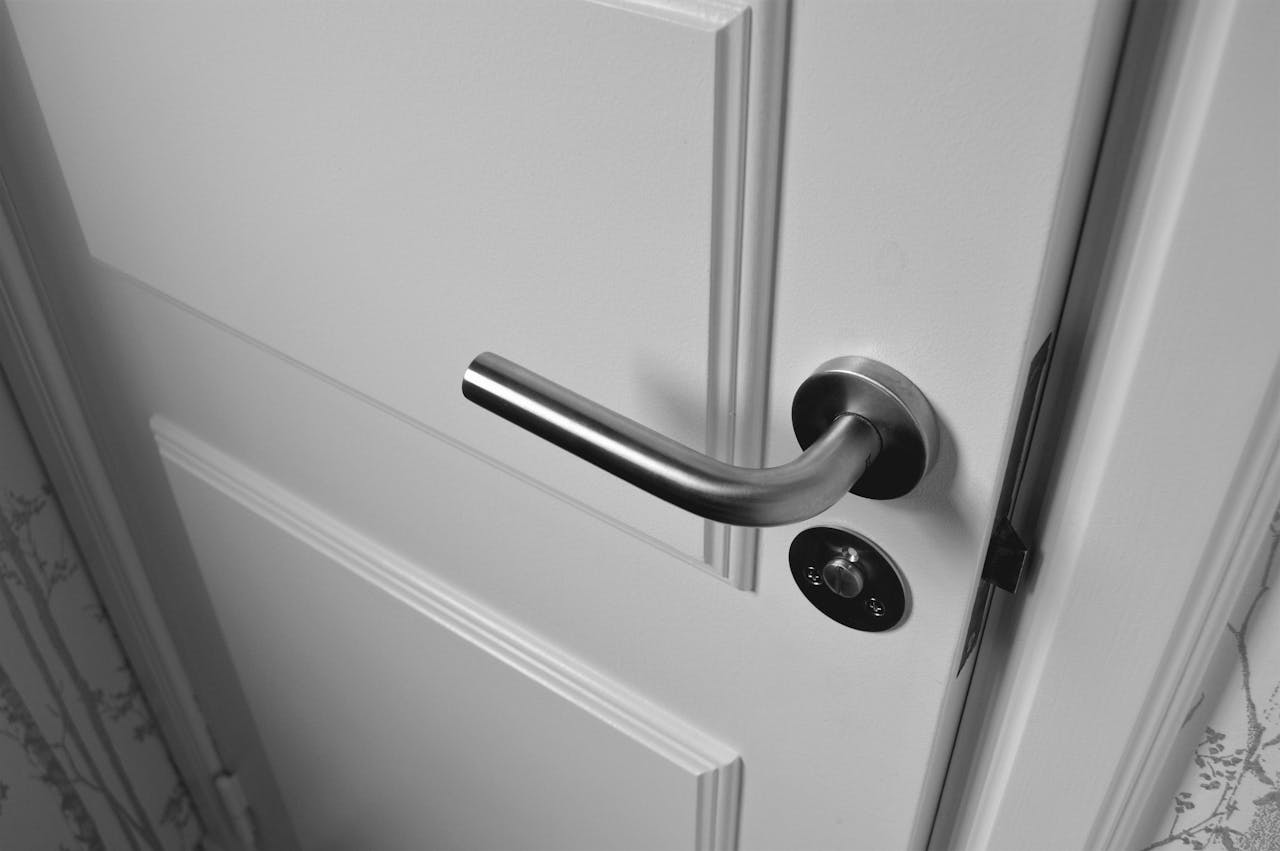 why-choose-us Close-up of a sleek steel door handle on a white door, showcasing modern interior design in monochrome.